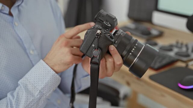 Man in light blue shirt points finger to camera dial while holding mirrorless lens in studio; concentrated practice.