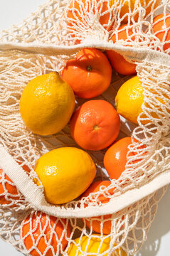 Lemons and tangerines in eco-friendly shopping bag on light gray background, flat lay top view. Mesh cotton string bag filled with citrus fruits. Concept of eco-friendly living, zero waste