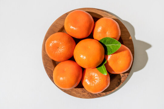 Fresh delicious tangerines with green leaves in wooden plate on light gray background. Orange tangerines, citrus fruit. Summer background with tangerines, top view, space for text