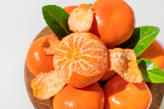 Fresh delicious tangerines with green leaves in wooden plate on light gray background. Orange tangerines, citrus fruit. Summer background with tangerines, top view