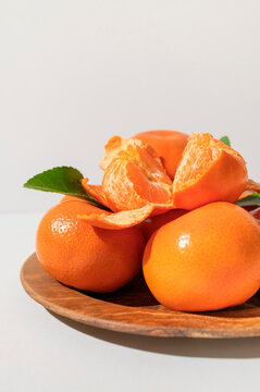 Fresh delicious tangerines with green leaves in wooden plate on light gray background. Orange tangerines, citrus fruit. Summer background with tangerines, top view, space for text