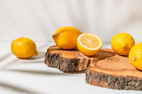 Yellow ripe lemons lie on wooden podium with sunny shadow from tropical leaf on white background. Summer background with lemons, citrus fruit source of vitamin C. Lemon mockup