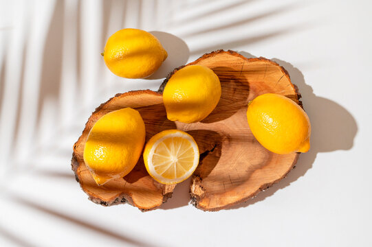 Yellow ripe lemons lie on wooden podium with sunny shadow from tropical leaf on white background. Summer background with lemons, citrus fruit source of vitamin C. Lemon mockup