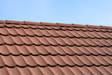 Naklejka premium An array of brown stone coated metal tiles covers a roof under a clear blue sky creating a textured repeating pattern