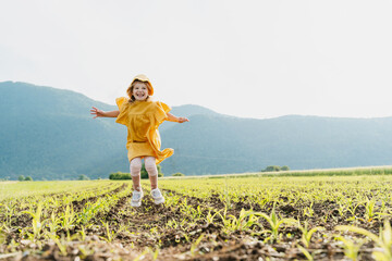 Fototapeta premium Little girl among agricultural field of young corn plant. Farm tourism or ecology concept.