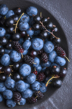 Close perspective of blueberries and mulberries in bowl, rich dark tones. Fresh summer berries, natural food styling
