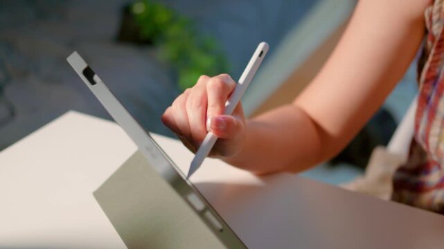 Close-up of female hands writing on digital tablet with stylus pen. Woman using touchscreen device for note taking, drawing, or online work in modern