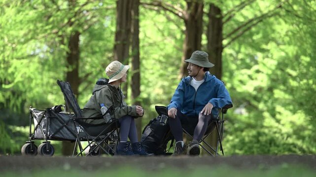 新緑のキャンプ場で椅子に座る笑顔のアウトドアやレジャーを楽しいミドルの夫婦　楽しく会話をするシーンの動画	