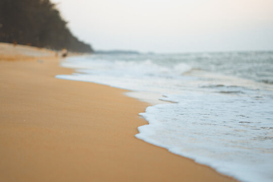 Beautiful sea waves with white foam washing onto golden sandy beach at sunset. Low-angle shoreline view captures a peaceful nature atmosphere, ideal for summer travel, vacation, and wellness concepts.