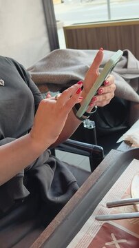 Close up of female hands with red nail polish holding mobile phone. Beauty and fashion detail showing manicure and digital device interaction at restaurant table
