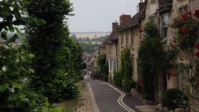 Sunny quiet uphill village street lined with stone houses and geraniums