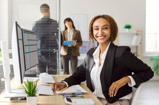 Smiling businesswoman accountant in office with computer. Confident professional reviews spreadsheets and prepares a financial report in a bright workplace. Portrait conveys trust and reliability.