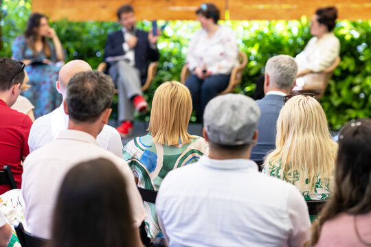 Outdoor business conference with roundtable where a professional audience follows a presentation in a green garden setting, as part of a sustainably organized corporate event