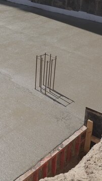 Vertical video. Fresh wet cement hardening and solidifying on a construction site, creating a durable concrete foundation for a new building as the shadow of a steel rebar moves across the surface
