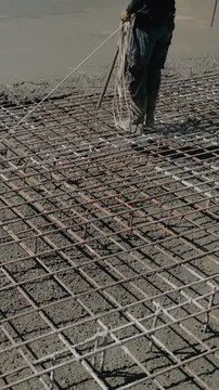 Vertical video. Construction worker using a poker vibrator to consolidate freshly poured wet concrete over a steel rebar mesh, ensuring a solid and compact foundation for a new building