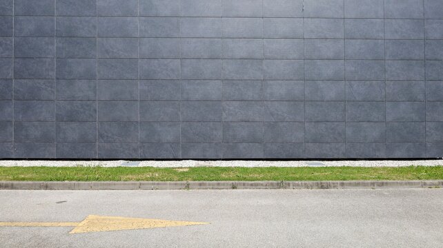 Gray stone tiles coating of a ventilated facade at roadside with grassy sidewalk and street in front. Background for copy space.