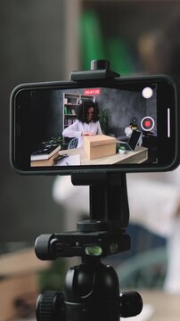 A woman films herself unboxing a package while giving a thumbs up, capturing content for her online channel