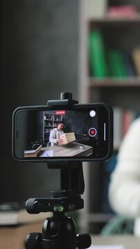 A man is recording himself on a smartphone while holding a cardboard box, likely for an unboxing or review video
