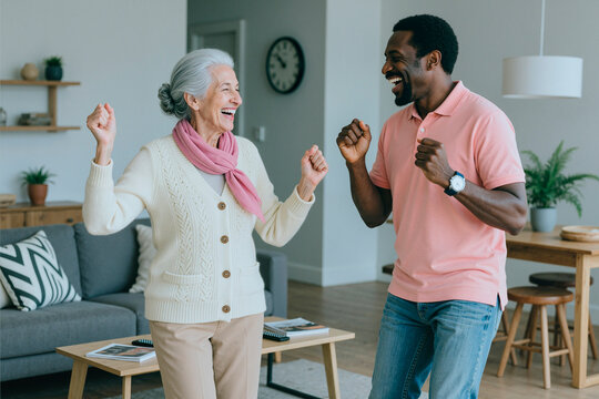Senior Caucasian woman and African American young adult man dancing together at home, smiling and exercising for active aging and family care. Useful for caregiving, wellness, support services