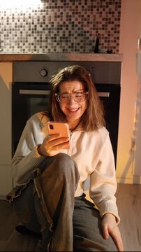 Vertical screen young woman laughs at phone message emotional release after tension mood shift from anxiety to relief lighthearted reaction in warm home space