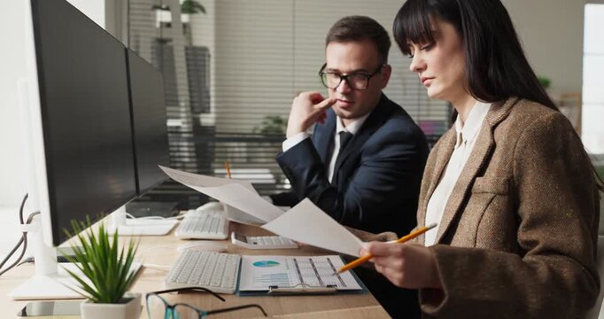 Business colleagues discuss financial analysis and teamwork. Side view of man and woman reviewing charts at office computer. They plan budgets and data reports. Clear concept of effective teamwork.