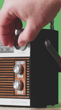 A person is tuning a vintage radio to listen to music. The radio has dials for different frequencies. The background is plain green and there is focus on the radio.