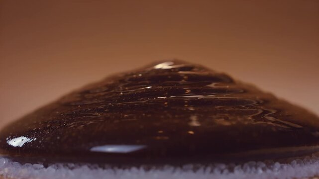 Dark chocolate syrup flows smoothly over a mound of granulated sugar, creating a glossy surface as it spreads and settles in a warm, softly lit environment
