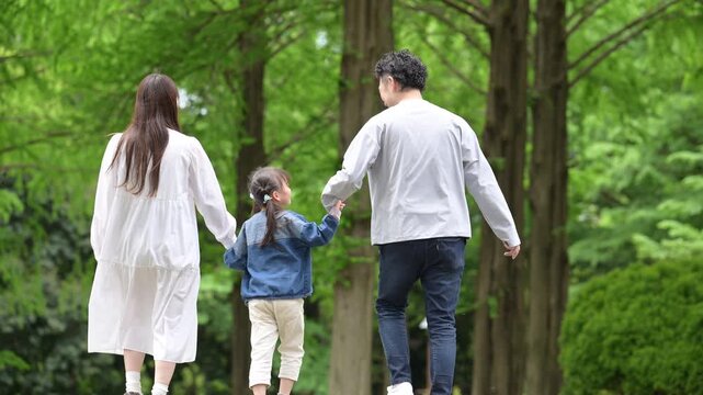 家族、新緑の公園で手を繋ぐ歩く幸せなファミリーライフスタイル動画　全身の顔無しの後ろ姿スローモーション
