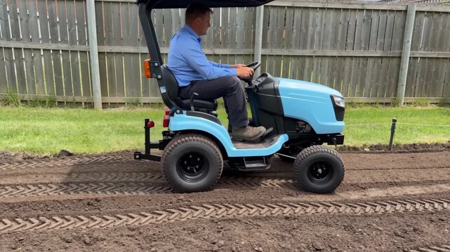 Man driving garden tractor preparing soil in backyard, ground leveling and cultivation work, home gardening, landscaping and small scale agriculture activity