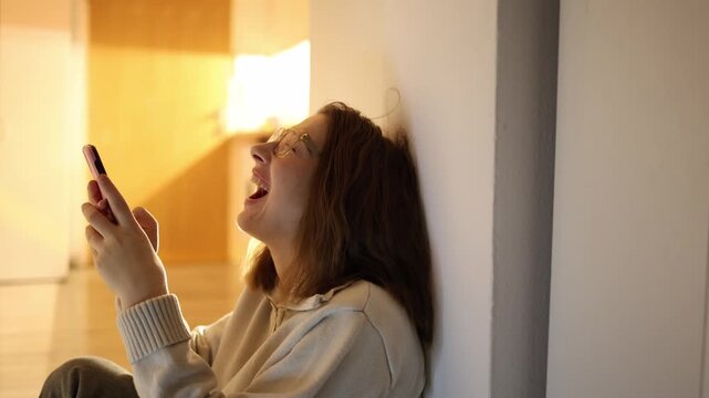 Young woman laughing at phone late evening enjoying funny content mood shift from sadness to joy relaxed home space bright emotion and lighthearted moment