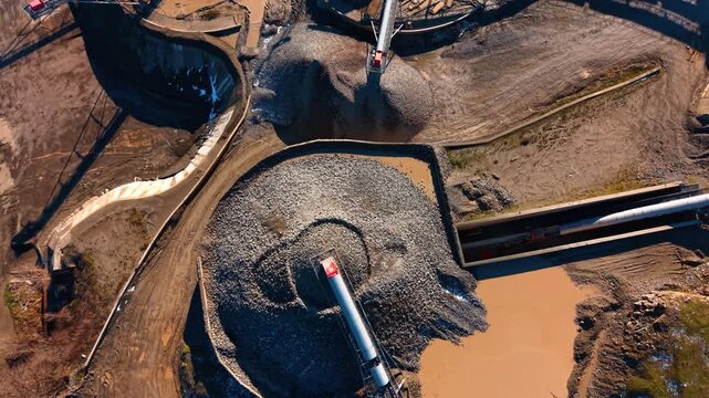 Top down aerial view of crushed stone storage pile. Circular pile of aggregate material being processed at a crushing plant with a conveyor belt and water pond.