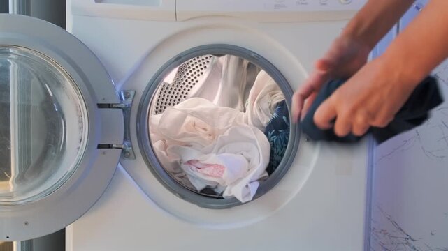 Woman placing white clothes into front load washing machine at home. Laundry routine, sorting light garments before washing, domestic chores, hygiene and everyday household cleaning process.