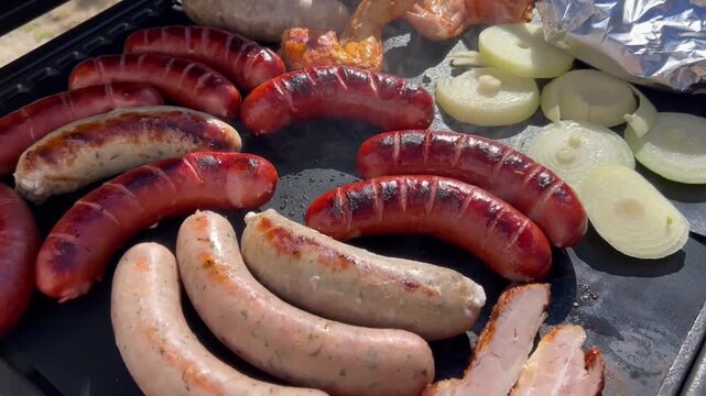 Close-up of sausages, chicken wings and onions grilling on a barbecue grate with smooth downward camera movement highlighting cooked food.