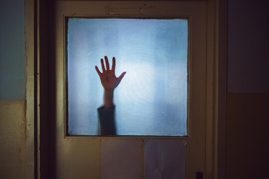 Hand of a woman sliding down stained glass door, eerie horror scene suggesting distress and confinement