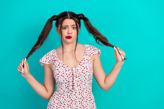 Young brunette woman with ponytails in a floral dress stands against teal background showing puzzled expression for fashion lifestyle stock photo