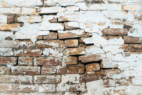 Texture of old damaged cracked weathered brick wall, thick layers of white paint are cracking, flaking and peeling of