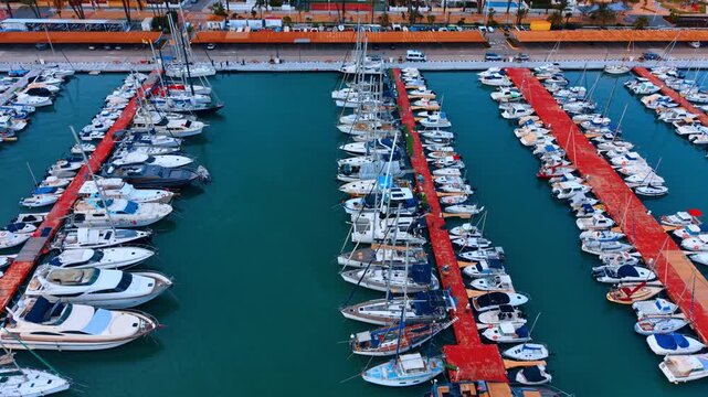 Symmetric aerial view of boats at red floating docks. High angle drone capture of parallel red piers with rows of white yachts in calm turquoise sea water.