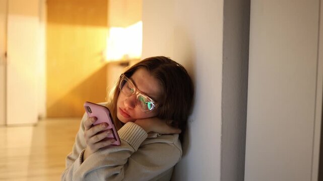 Woman sitting on floor at home scrolling smartphone instead of doing chores absorbed in endless content feed showing digital addiction low energy procrastination and loss of time