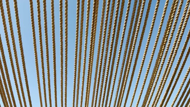 Dozens of rustic ropes stretch tightly overhead, creating a striking pattern. This unique canopy blocks the sun, offering a peaceful and airy feeling beneath the open, bright blue sky.