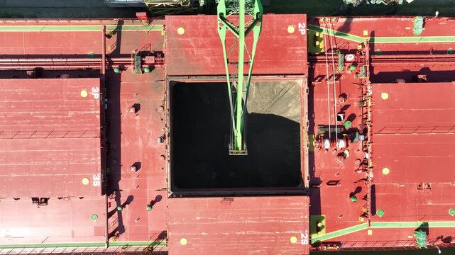 Unloading dry cargo ship of wheat by cranes in port. Aerial view loading into holds of sea cargo vessel