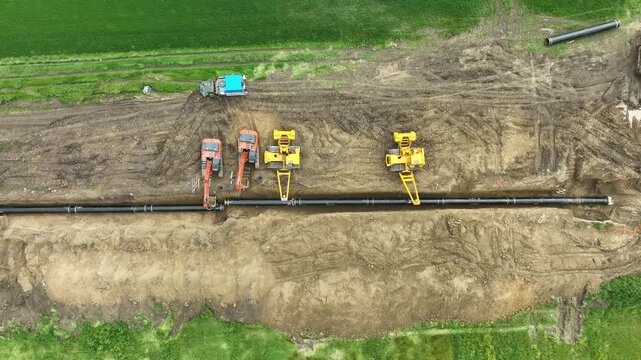 Aerial view of a major pipeline construction project. Heavy machinery including excavators and pipelayers install a new gas line in a rural field. Industrial energy infrastructure development.