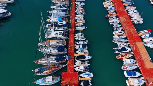 Luxury yachts moored at red pier. Top down drone image of numerous white motorboats and sailing yachts attached to a red marina pier.