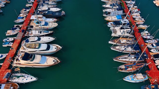 Aerial view of luxury yachts docked at a marina pier. High angle view of motorboats and yachts at a red pier in turquoise sea water.