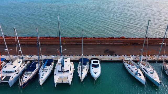 Sailing catamarans and yachts moored along a harbor pier. Row of sailing catamarans and yachts docked at a concrete pier near the open sea.
