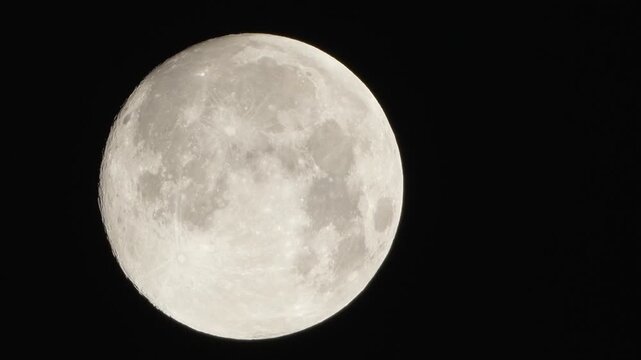A detailed close up shot of a glowing full moon showcasing its craters and surface texture against the dark night sky background.