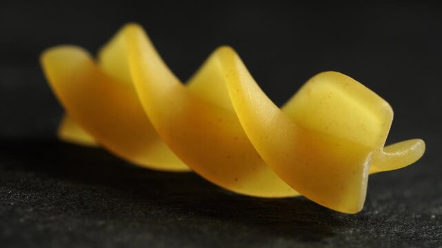 One fusili pasta slowly rotates on a dark stone surface, close-up, macro, texture.