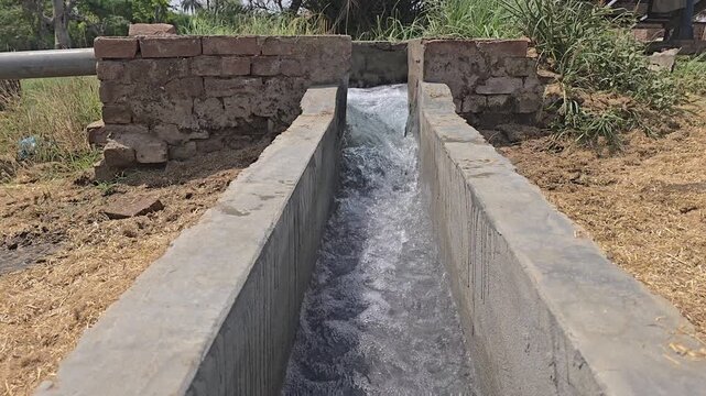 Agricultural irrigation water flowing through concrete canal, rural farming water supply system, traditional masonry irrigation channel in field