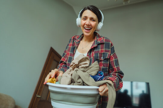 Smiling woman with laundry basket and headphones tidying up at home