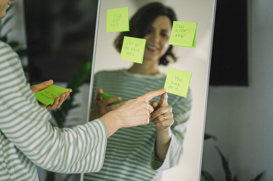 Pointing at positive affirmation sticky note on mirror indoors