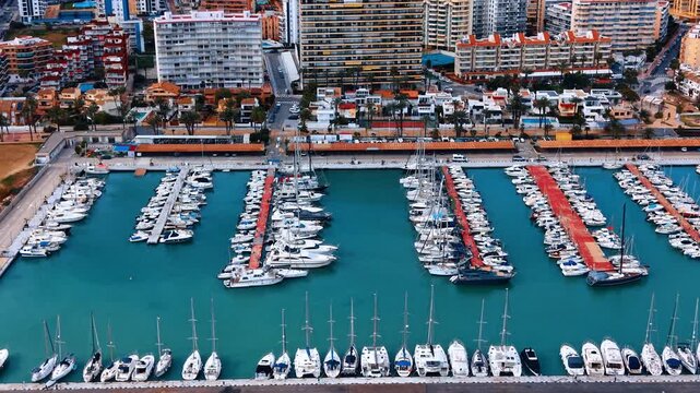 Rows of white luxury yachts in city marina harbor. Detailed aerial view of numerous boats moored at organized docks in turquoise water.